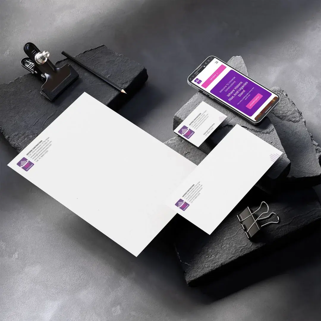 Universe Constructions - corporate stationery flat-lay on dark stone: letterhead, envelope, business card, and brand applied on a mobile site mockup